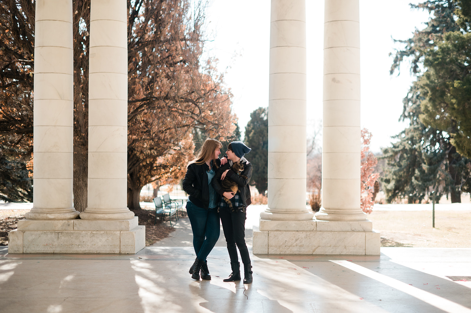photo of two women standing next to each other between two columns at Cheesman Park while holding their cat
