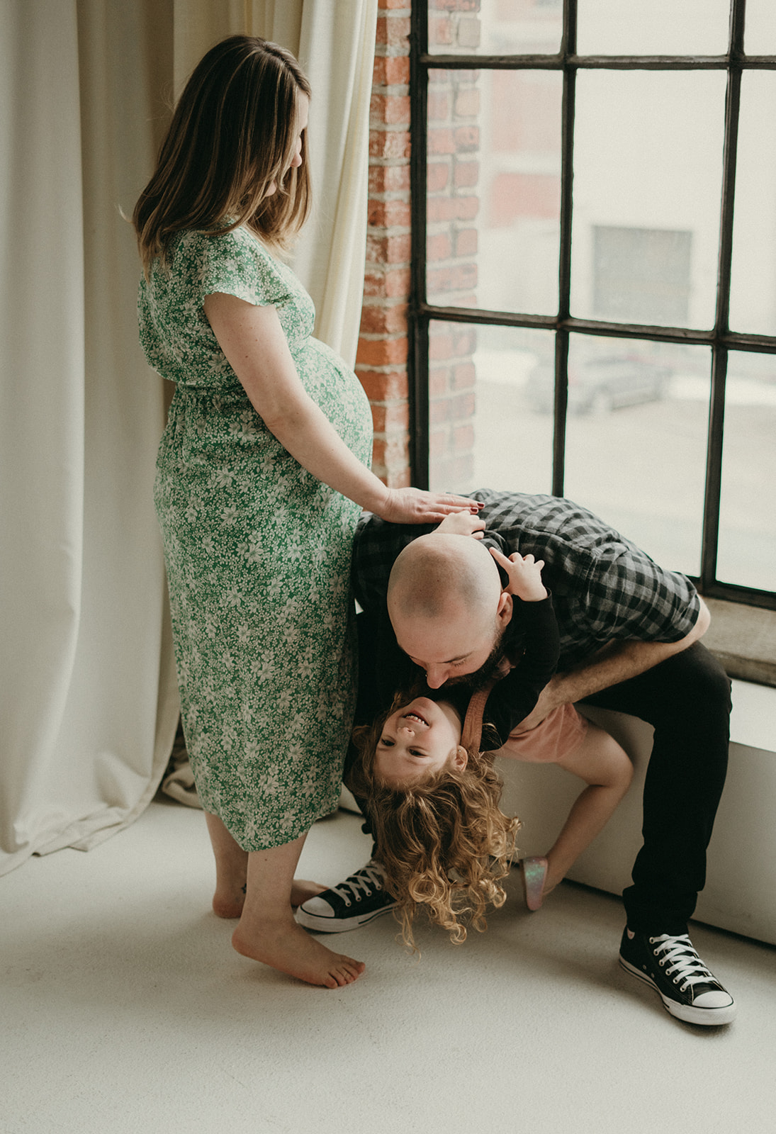 Pregnant mother, her husband and their three-year-old laughing and playing together