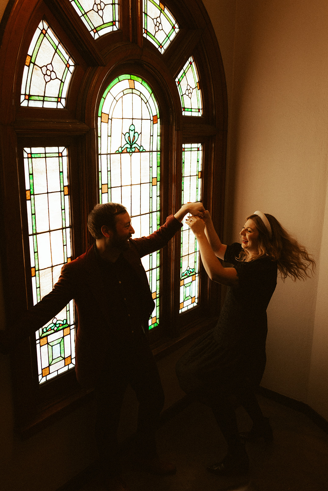 engaged couple spinning around and dancing in front of stained glass window