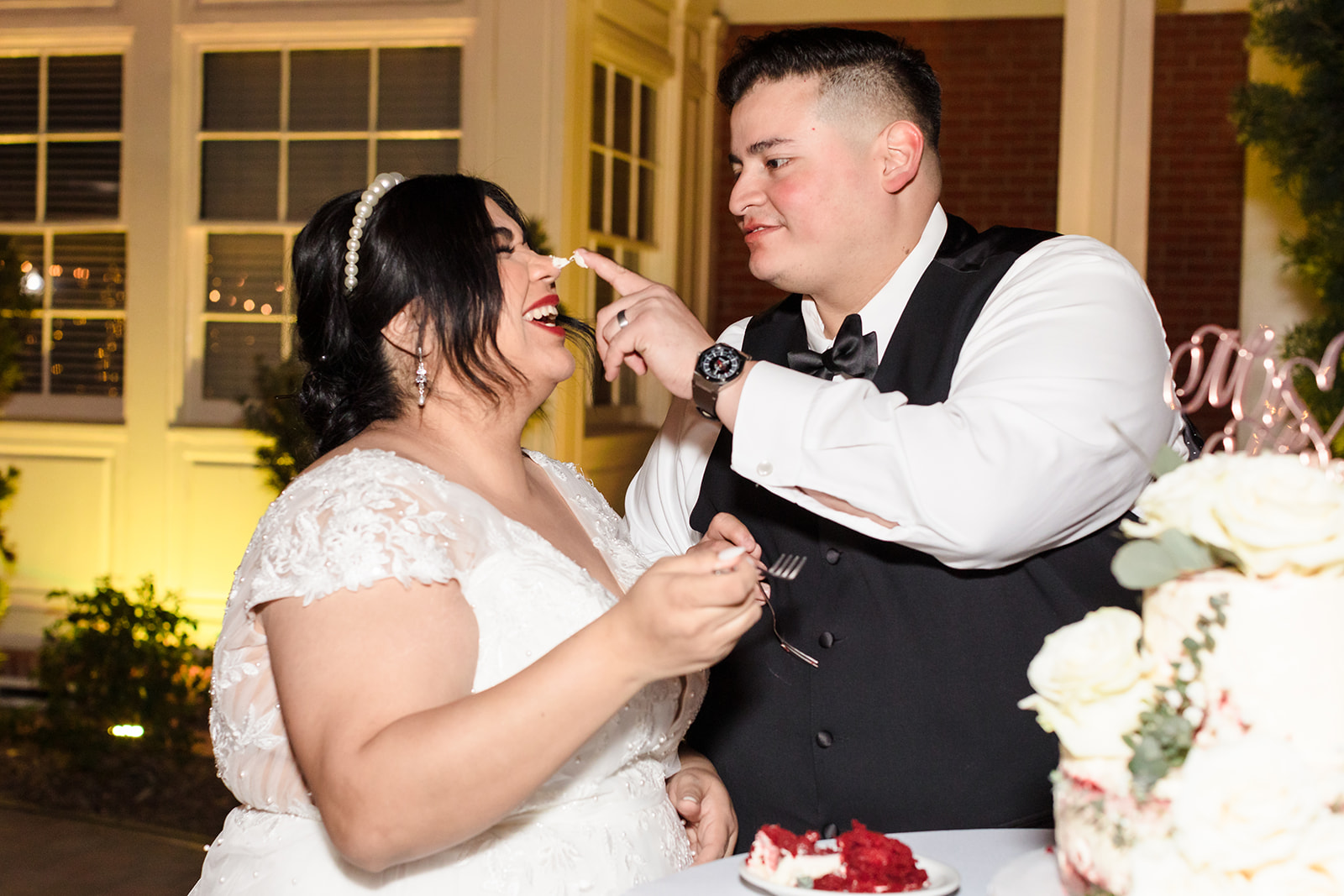 The groom smears cake frosting on the bride's nose and she laughs as they cut their wedding cake