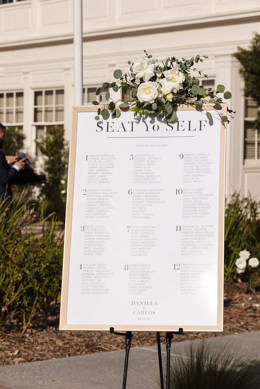 Gold framed guest seating chart with white florals on an easel