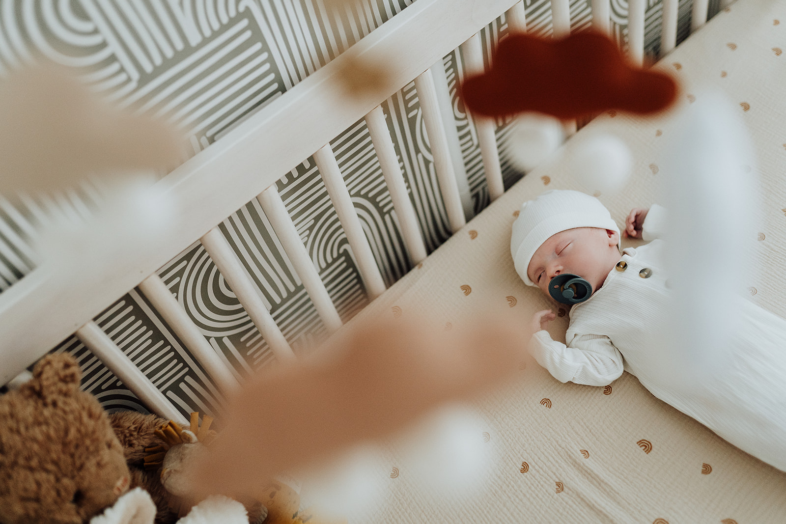Baby in white sleeping in his nursery crib as the cloud mobile hangs above 