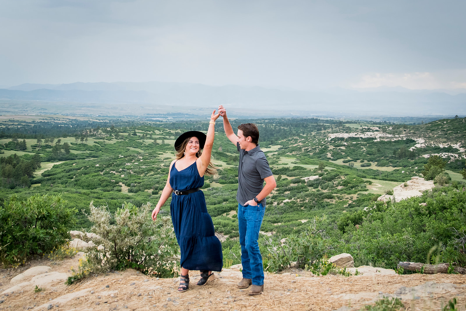 Couple dances on the edge of a scenic overlook as man twirls woman.