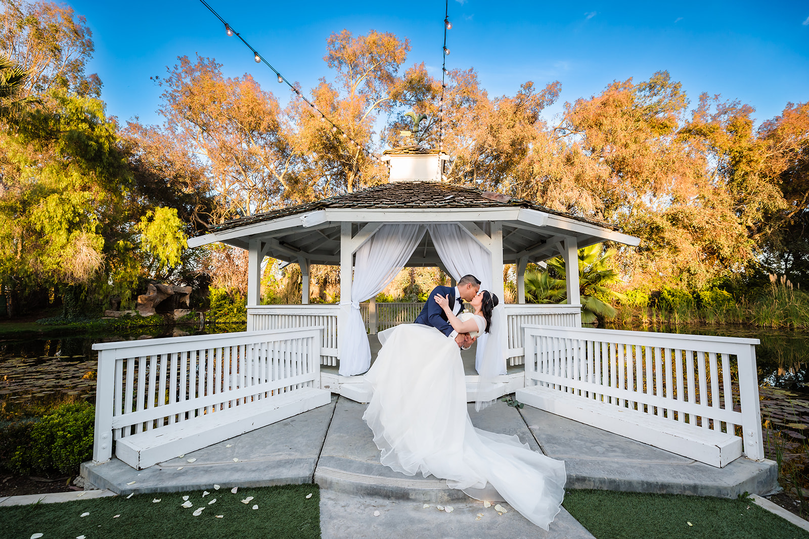 Groom dips his bride for a kiss in front of the gazebo at The Orchard by Wedgewood weddings in Menifee, CA