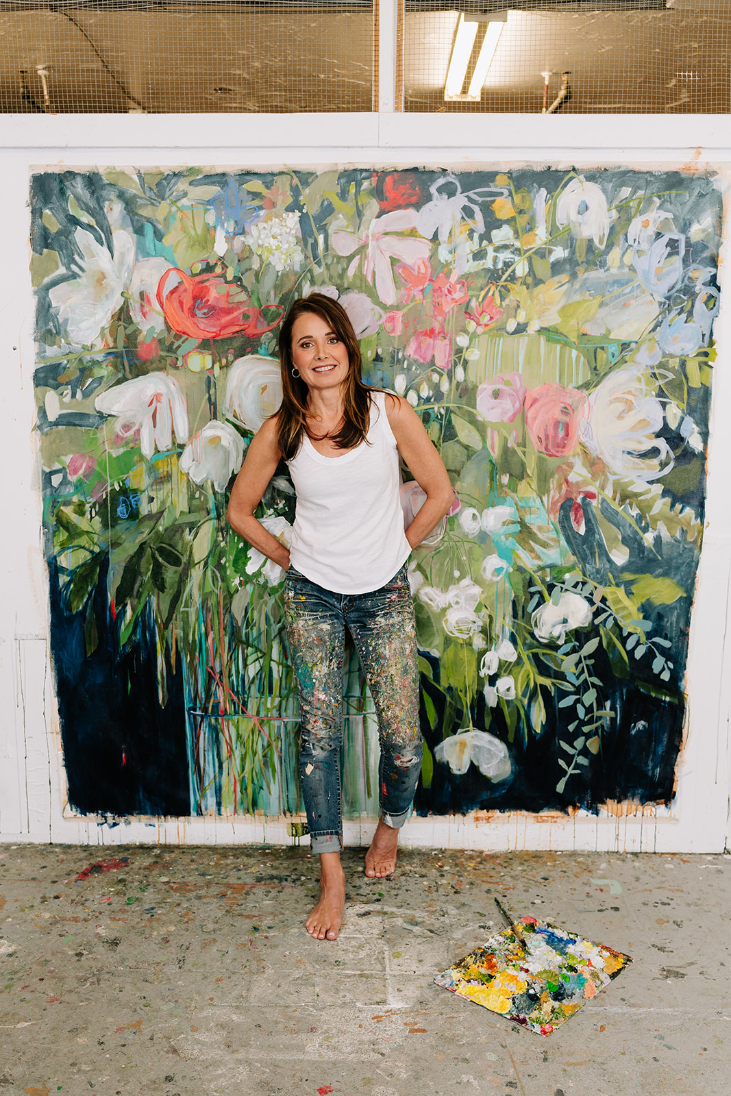 woman leaning against floral canvas painting in painted jeans