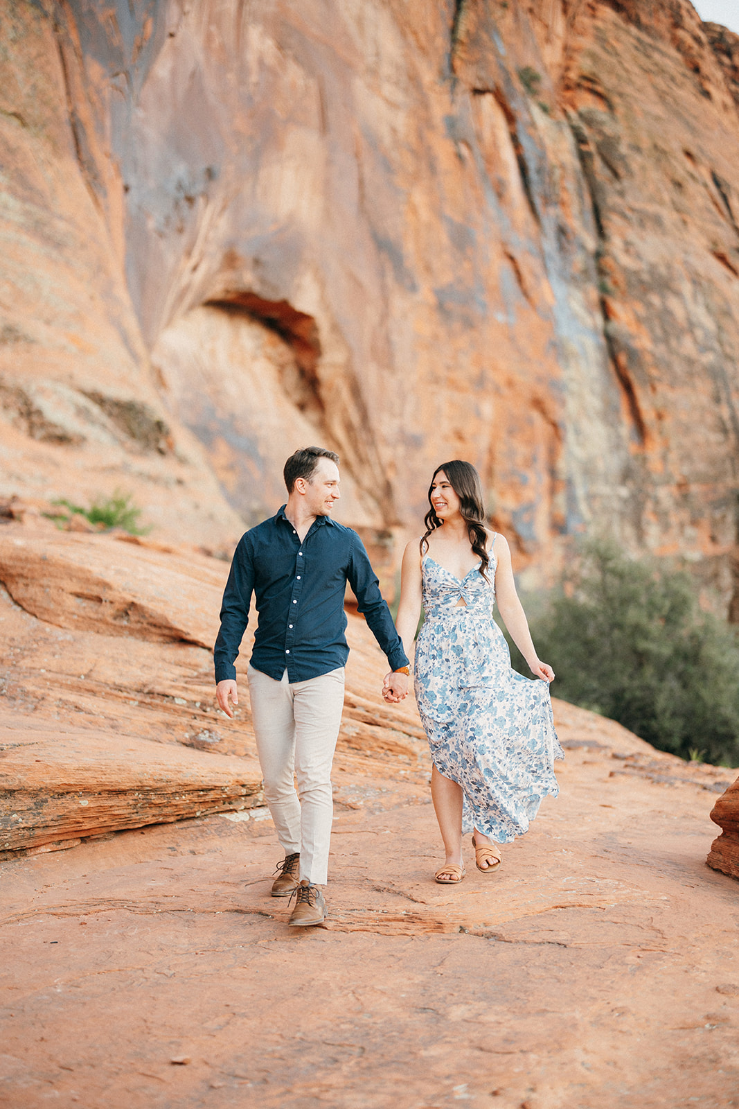 engaged couple runs down red rock cliffs
