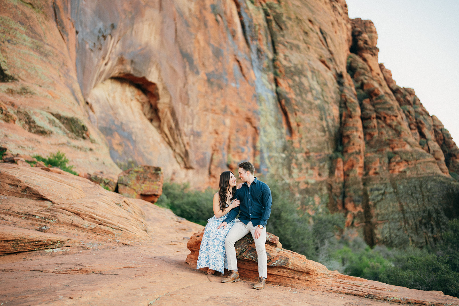 engaged couple sits in front of cliffs