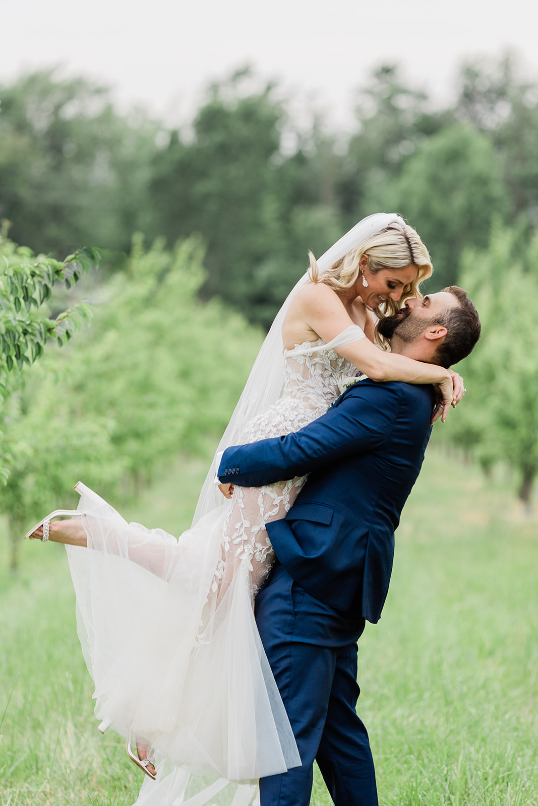 groom lifting bride in orchard at farm to table wedding by jess collins photography