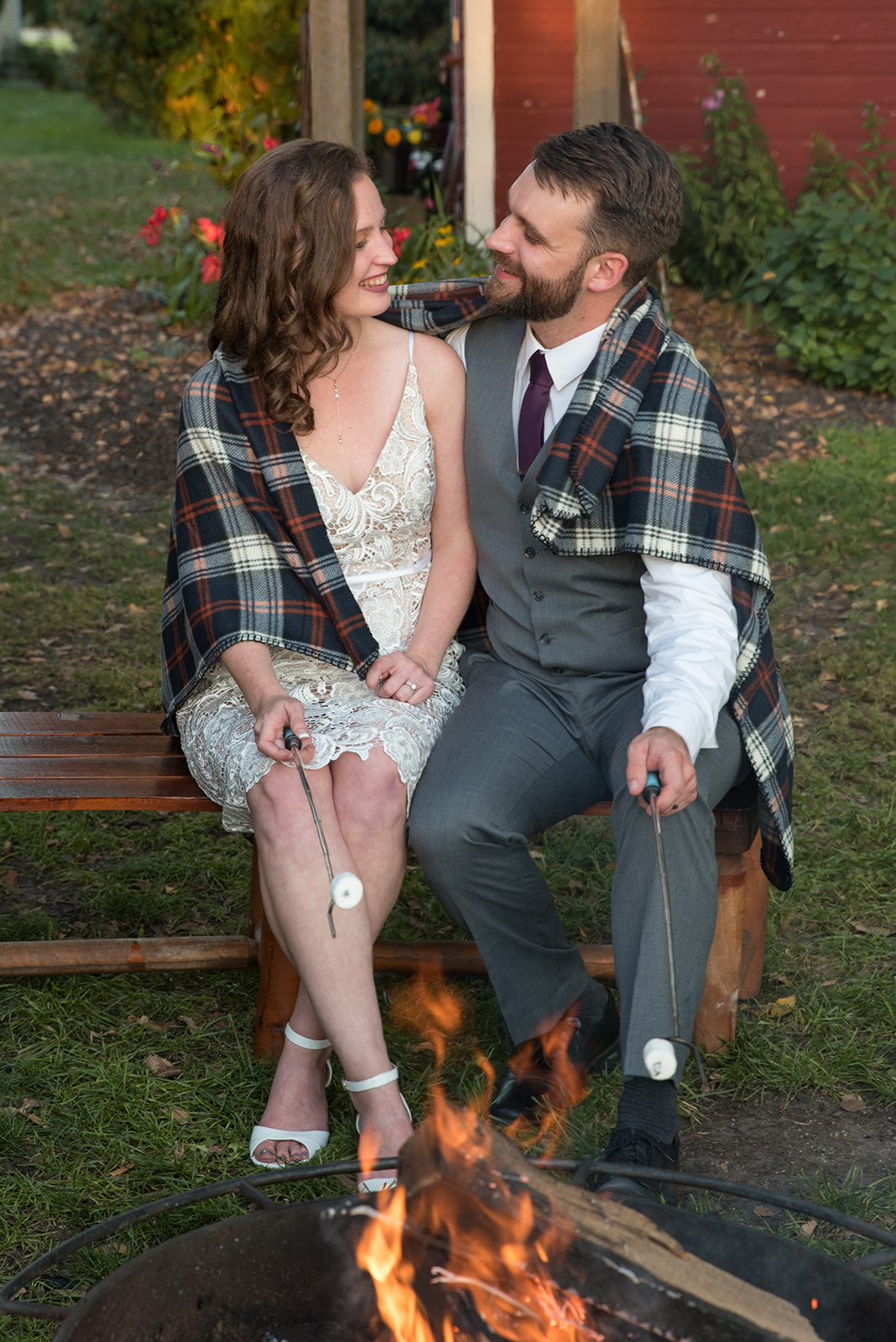 Bride and groom roast marshmallows over a fire while wrapped in a flannel blanket at Erickson Farmstead in Minnesota