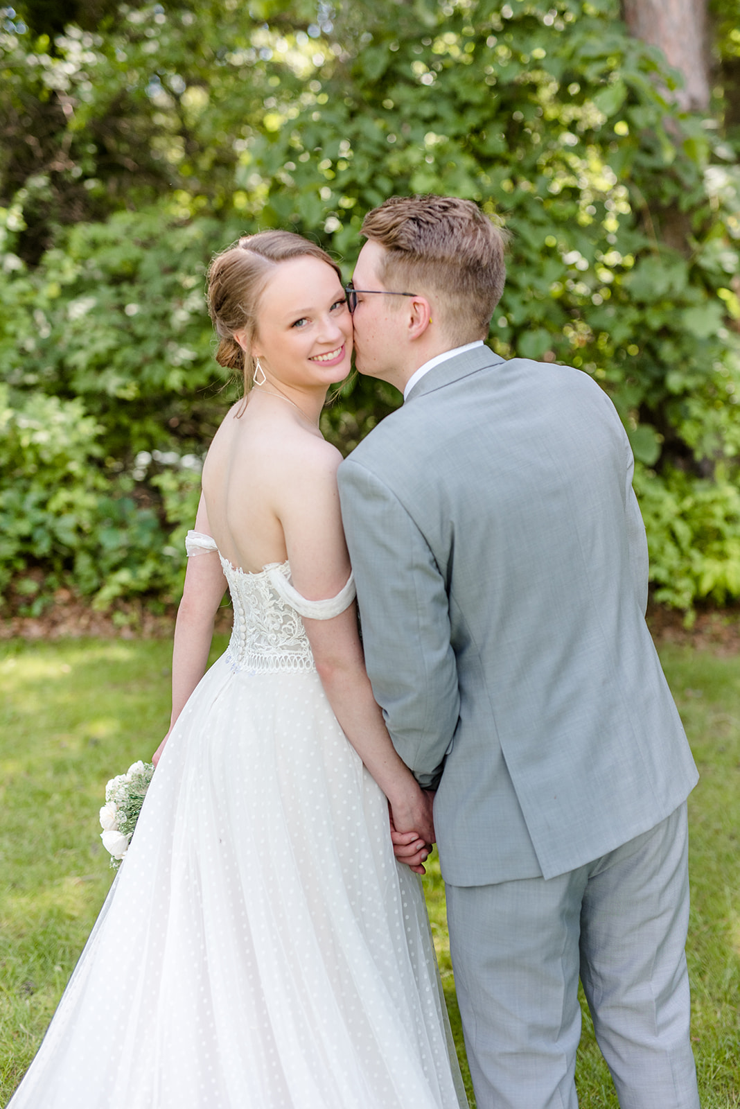 Bride looks back over her shoulder while the groom kisses her cheek