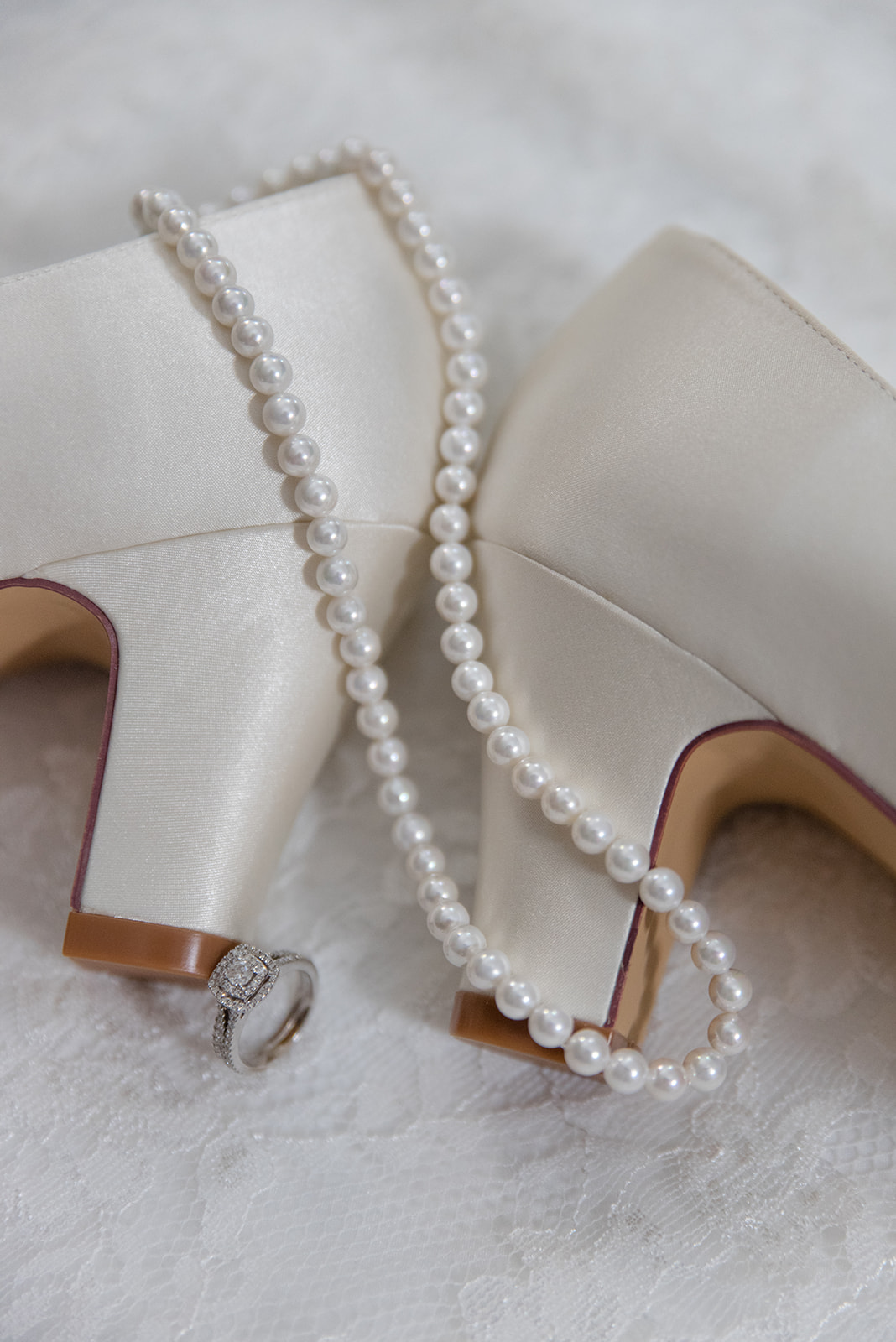 Close up on white heels with pearl necklace and diamond engagement ring