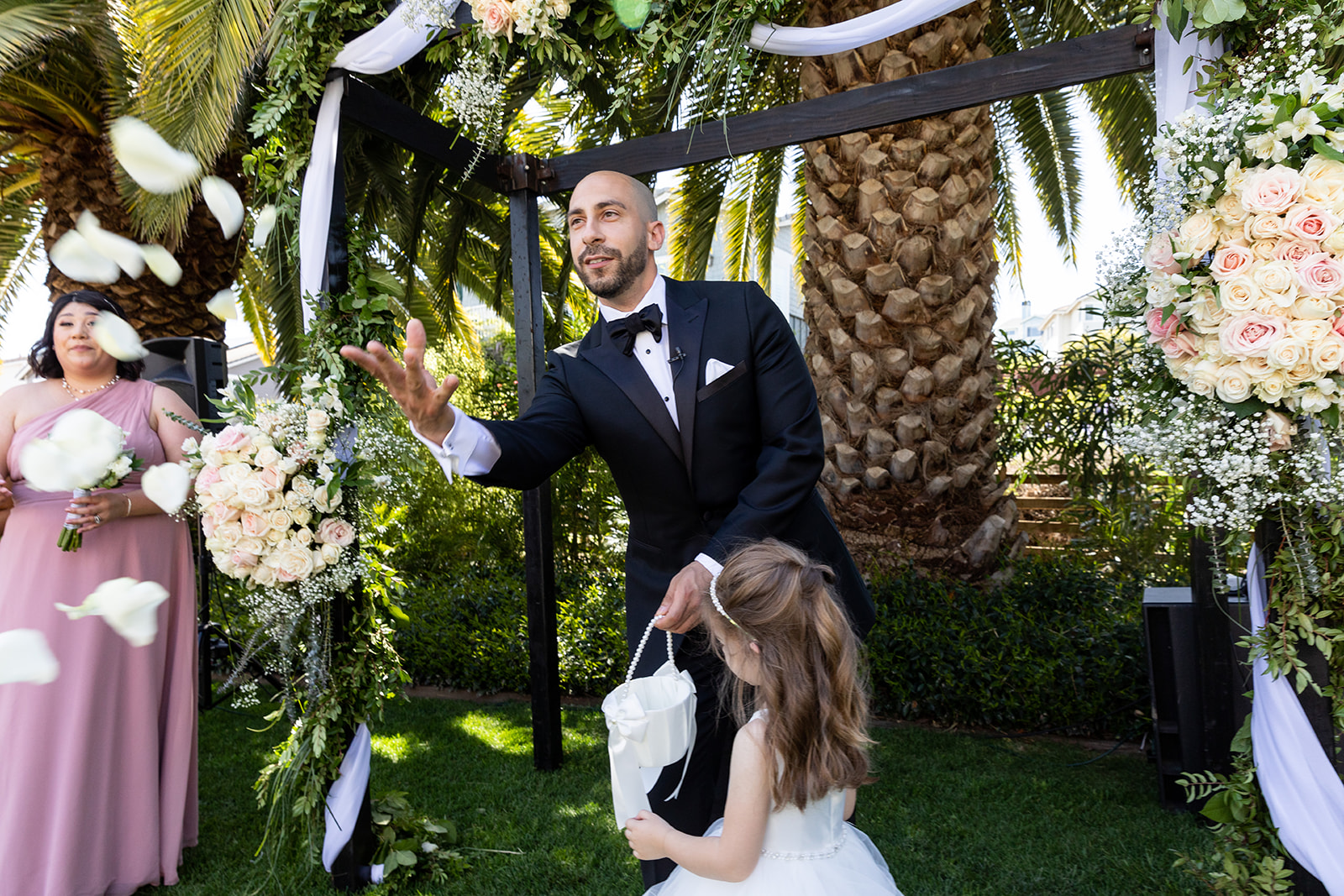 groom helps flower girl throw petals