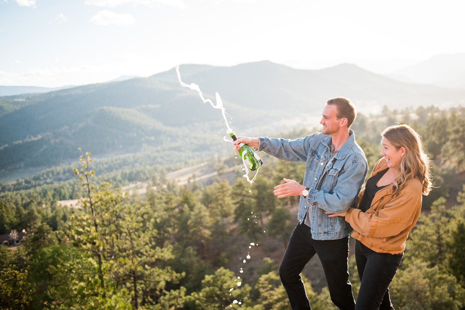 Man and woman pop a bottle of champagne on top of Mount Falcon.