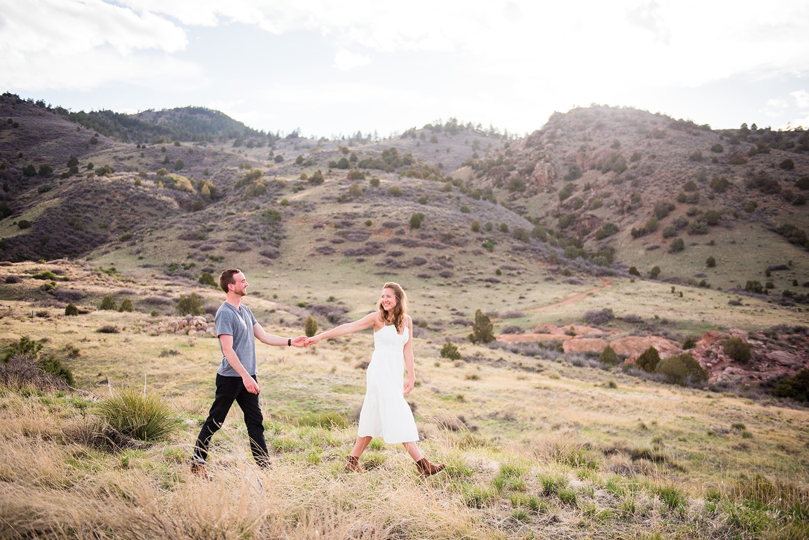 Woman leads fiancé through grassy field at Mount Falcon Colorado.