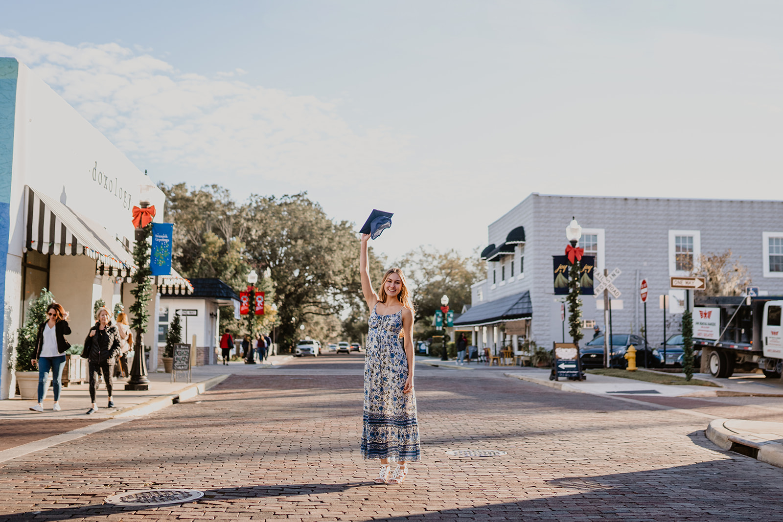 Wide angle view of Senior throwing 2023 graduation cap on cobblestone streets of Winter Garden, FL.