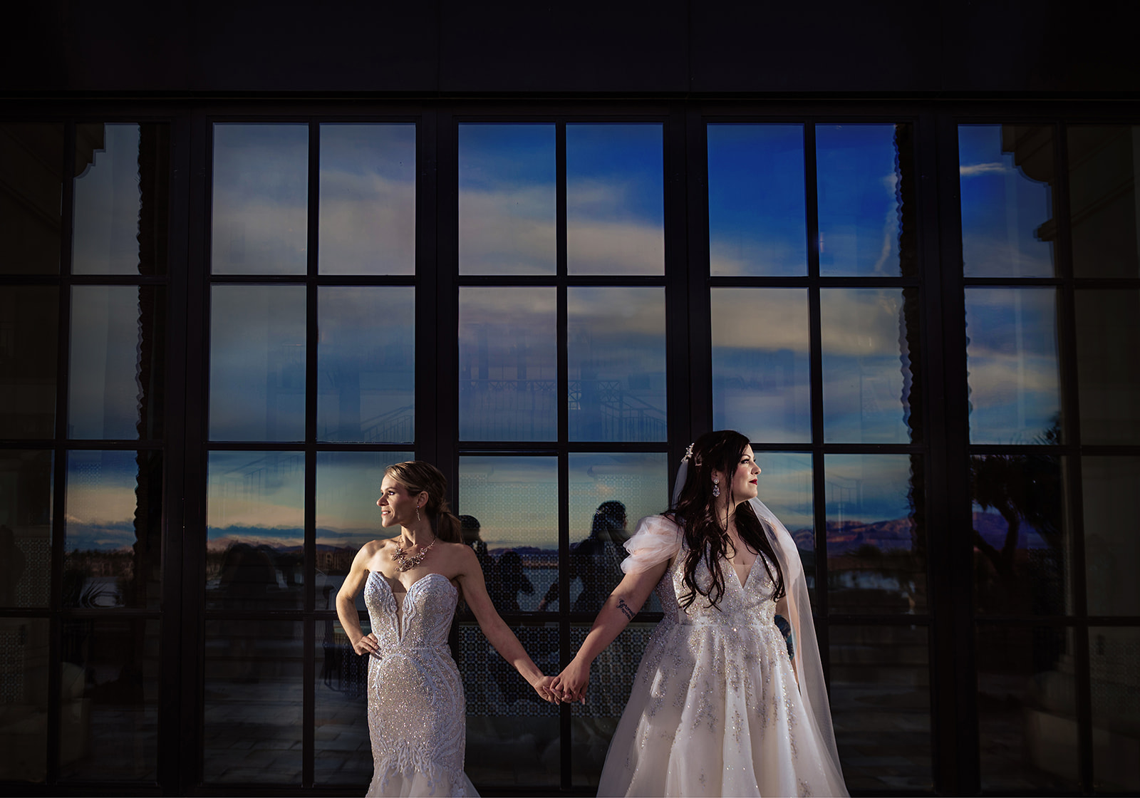 Two brides in colour photo holding hands in a moody portrait at their las vegas wedding. 