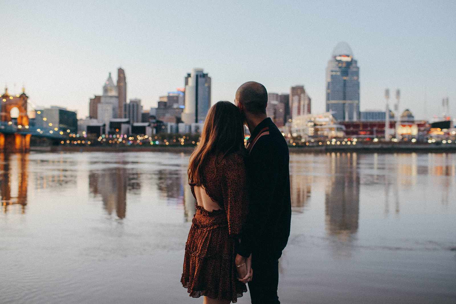A couple holds one another as they look over the Ohio River onto the setting sun of their hometown of Cincinnati